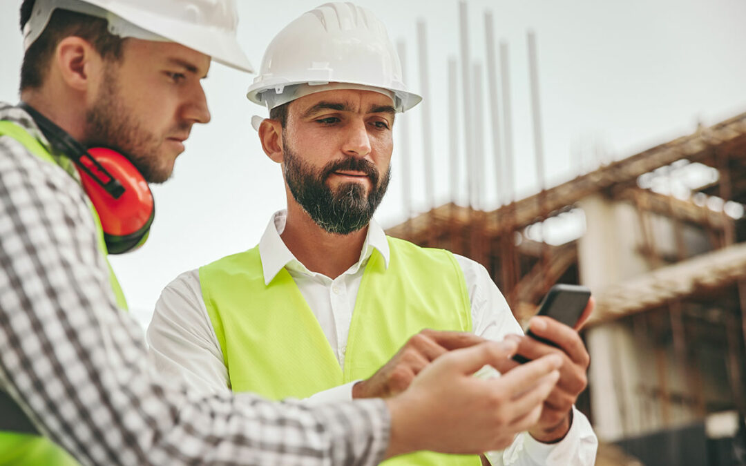 Zwei Bauingenieure stehen auf der Baustelle und schauen gemeinsam auf ein Smartphone